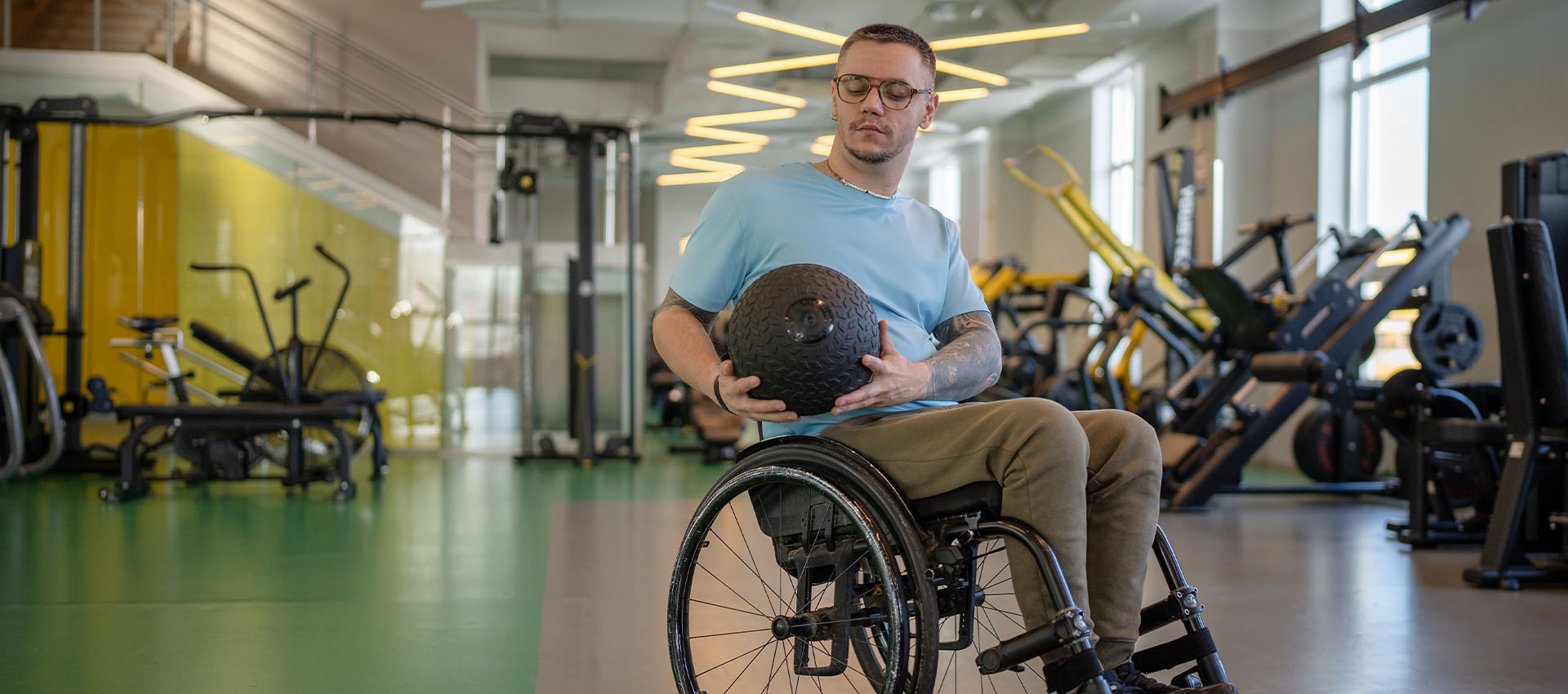 Man in a wheelchair holding a medicine ball while exercising in a gym.