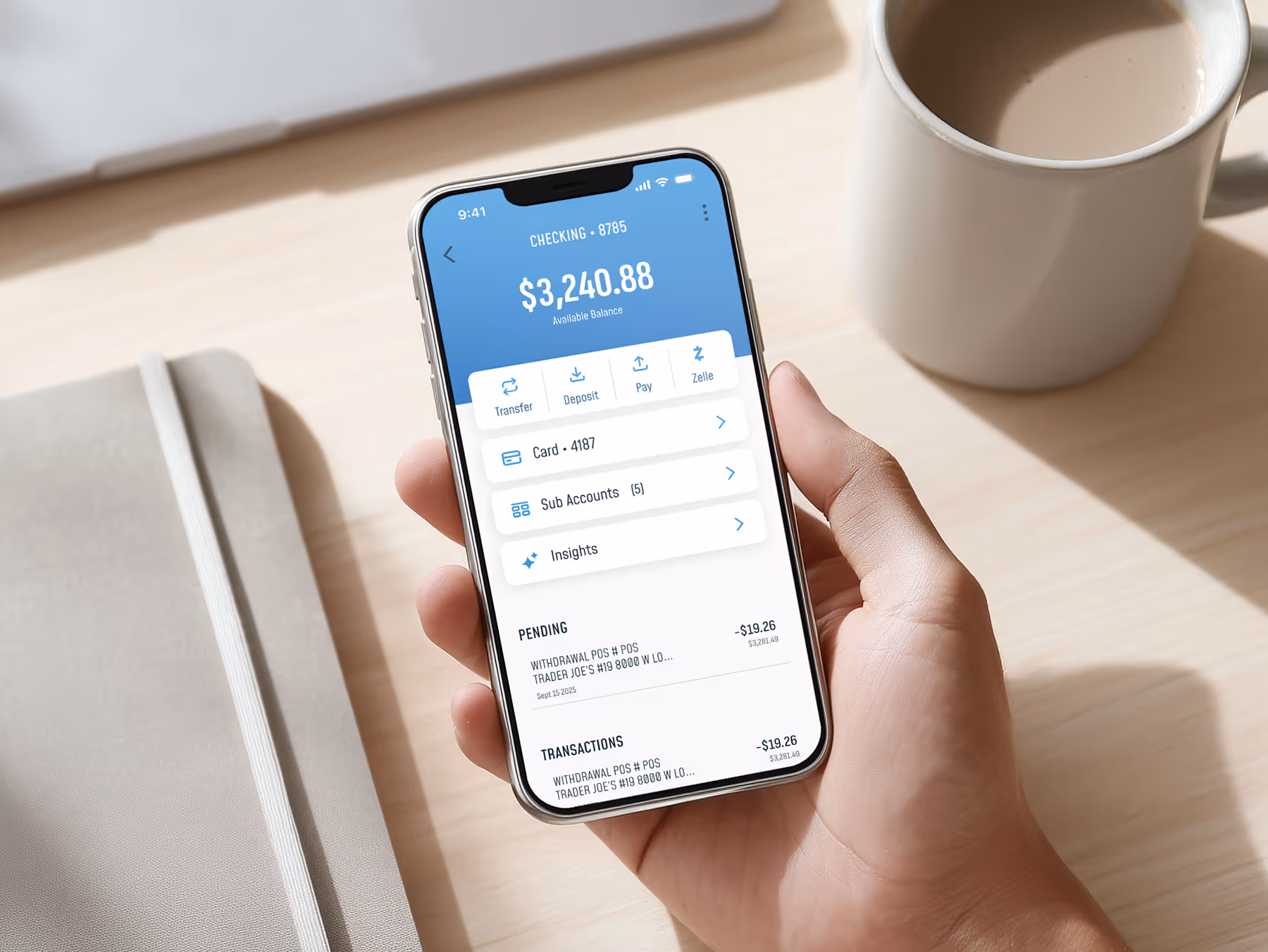 Hand holding smartphone displaying a banking app with a $3,240.88 checking account balance and recent transactions.