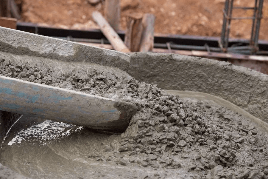 Close-up of wet concrete mixture with gravel being poured from a chute at a construction site.