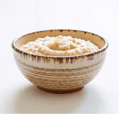 Rustic ceramic bowl filled with creamy mashed potatoes on a white surface.