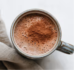 Top view of a cup filled with frothy hot chocolate topped with cocoa powder, next to a beige cloth.