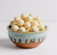 Ceramic bowl filled with white chocolate-covered round treats on a light background.