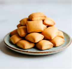 Stack of small, square, golden-brown biscuits piled on a round ceramic plate.