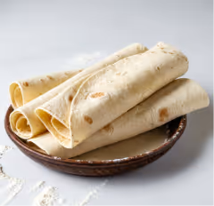 Stack of folded flour tortillas on a brown ceramic plate with a white surface background.