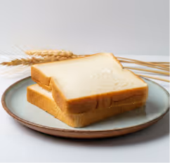 Two slices of white bread stacked on a ceramic plate with wheat stalks in the background.