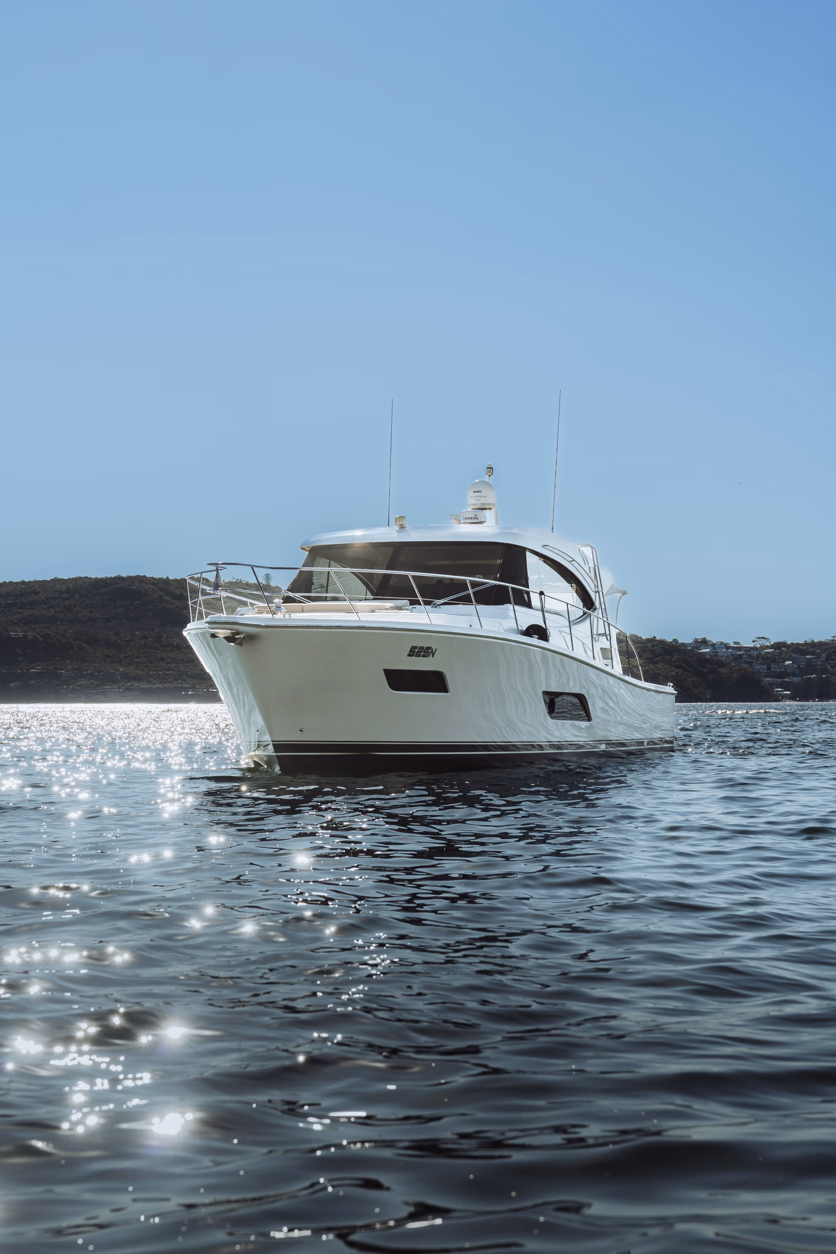 White motorboat cruising on calm water with sunlight sparkling on the surface and hills in the background.