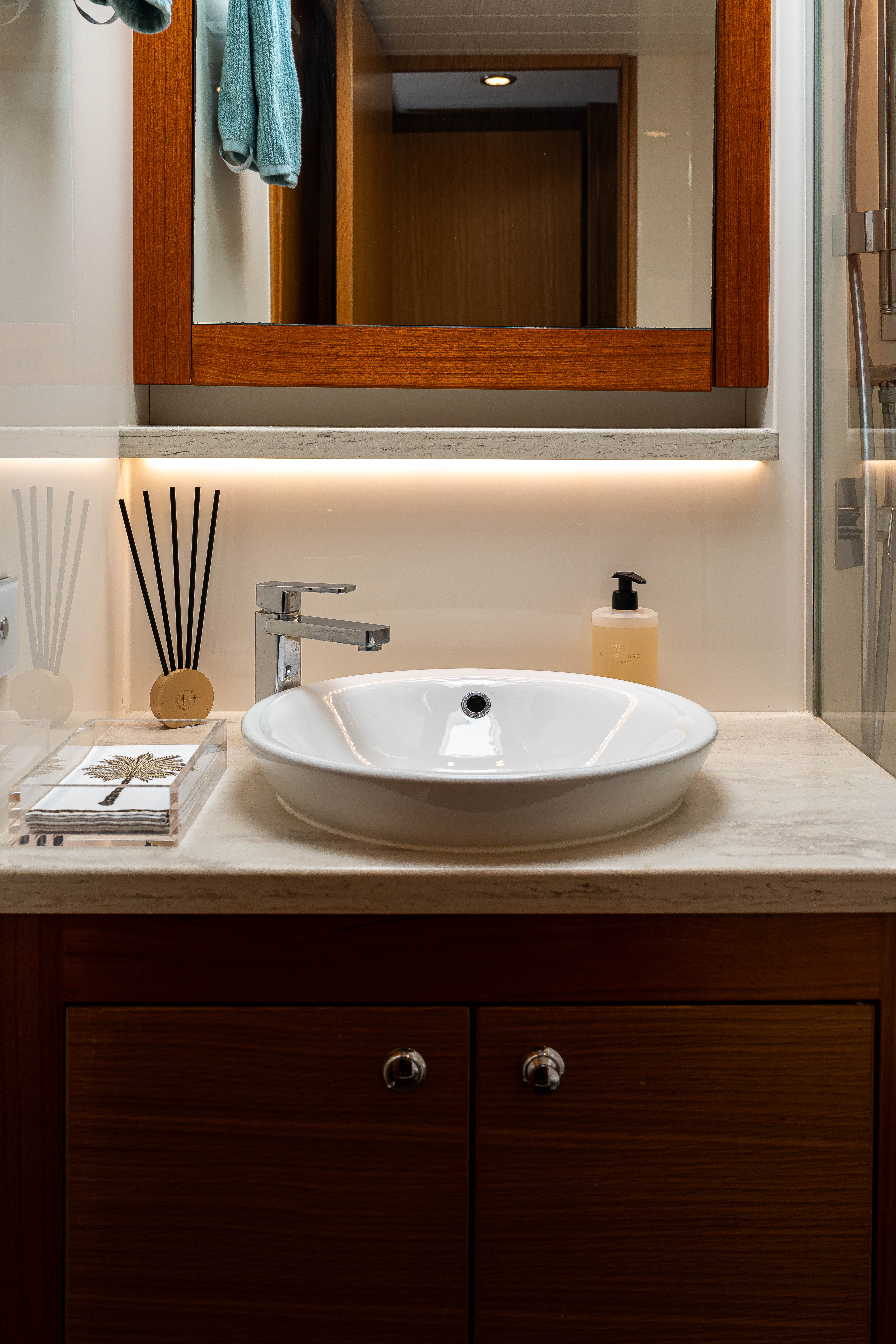 Modern bathroom sink with chrome faucet, soap dispenser, and diffuser under a wooden-framed mirror.