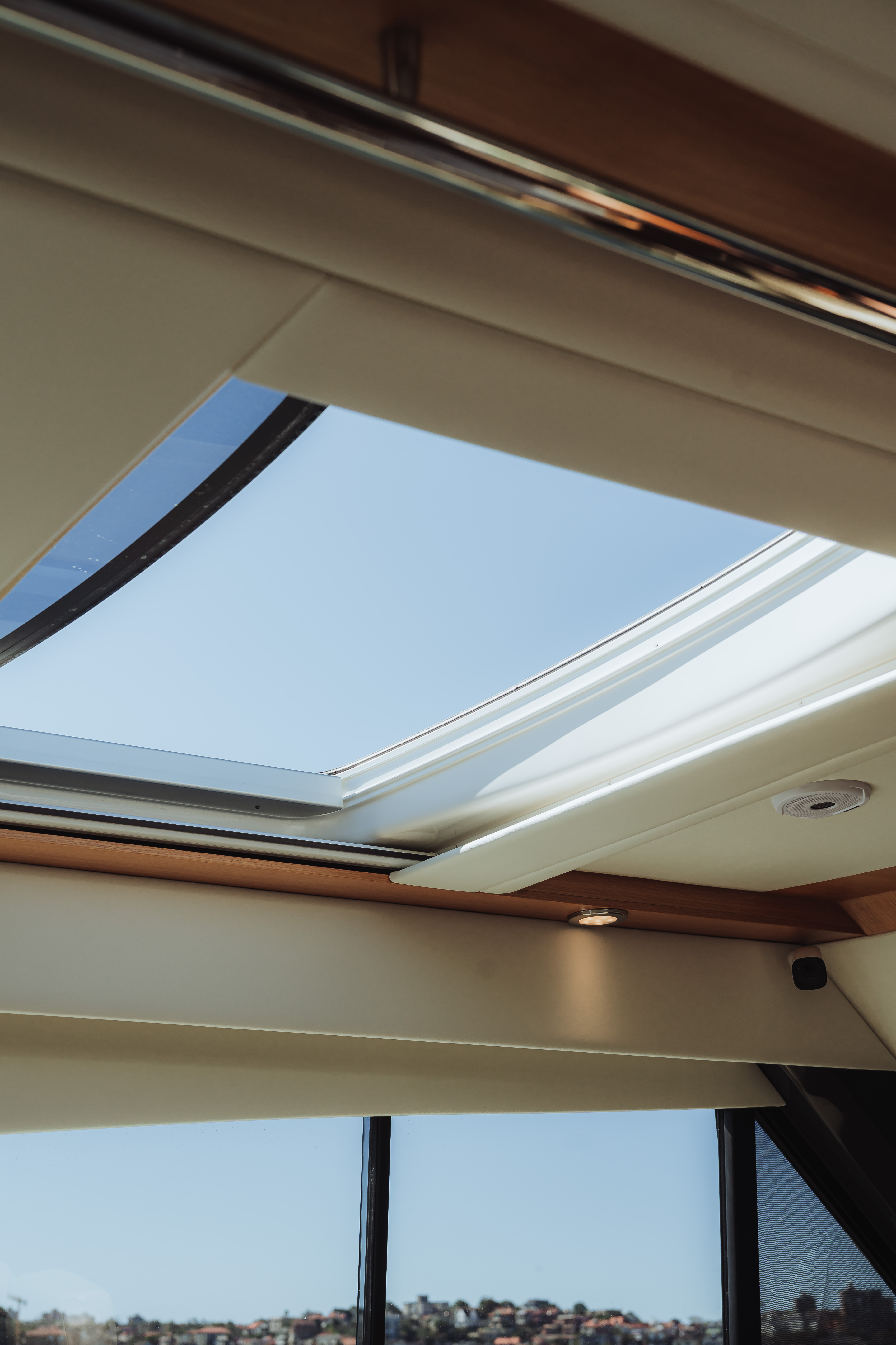 Partially open sunroof on a boat showing clear blue sky and distant shoreline.