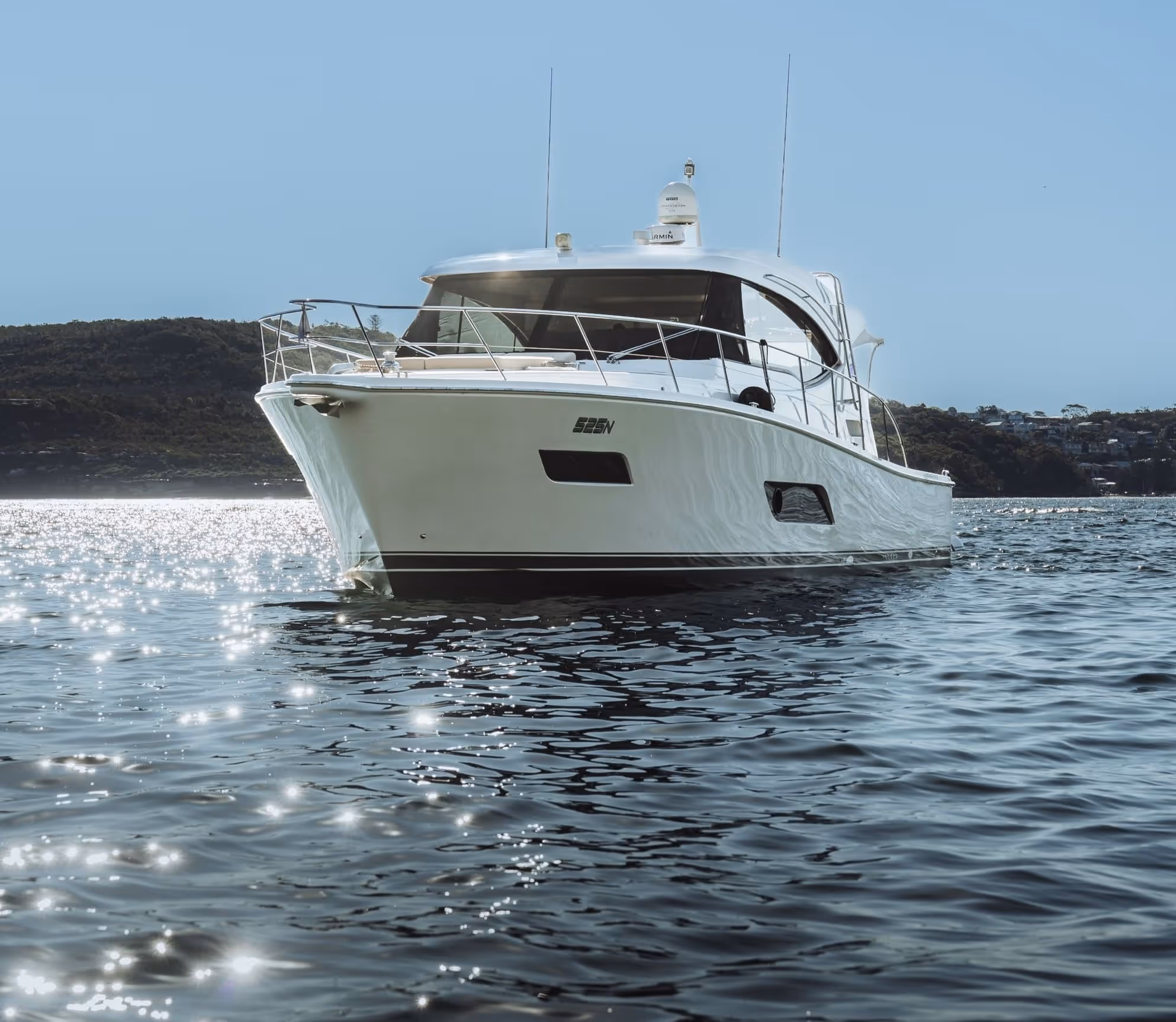 White luxury motor yacht on calm water with sun reflecting off the surface and hills in the background.
