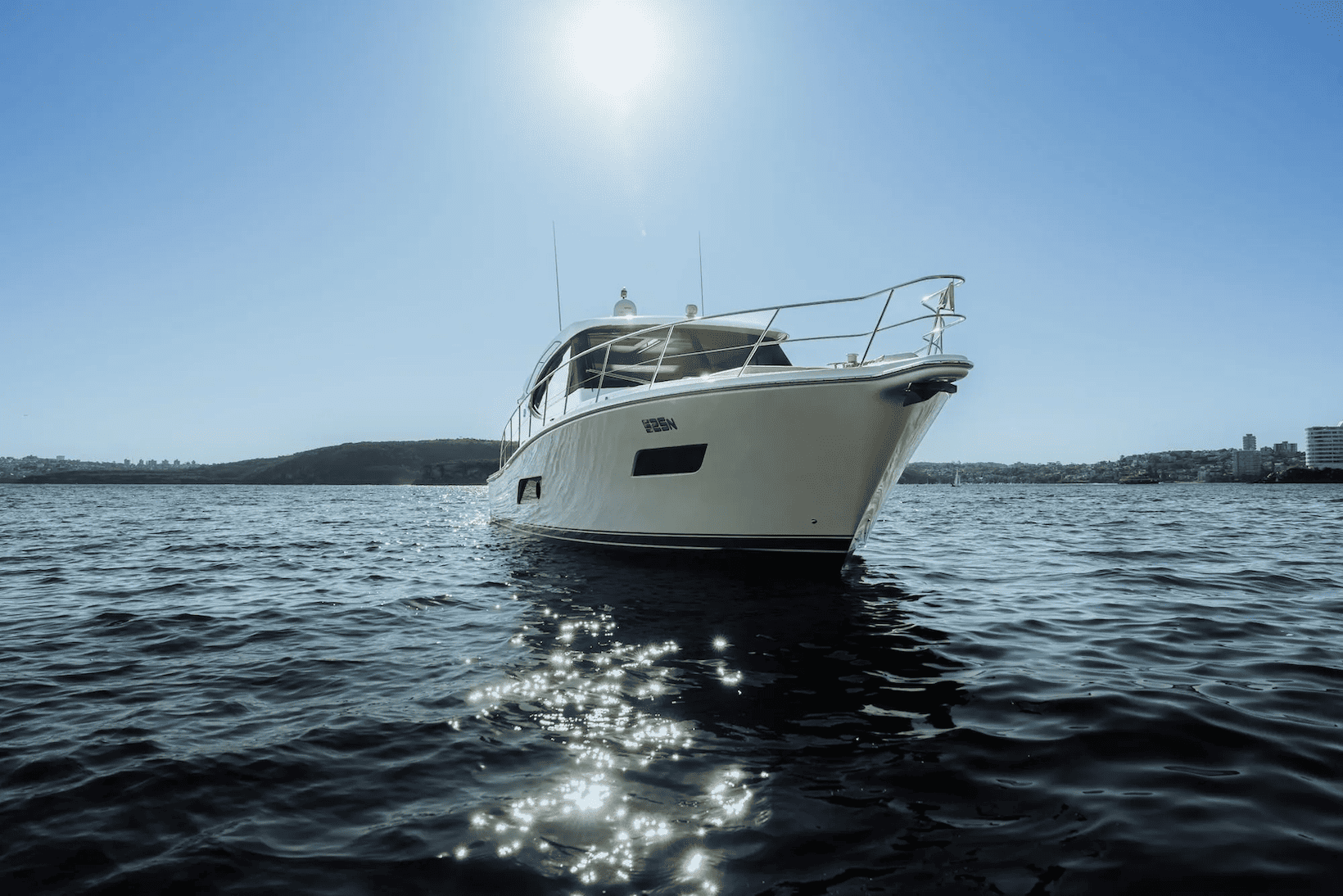 White yacht floating on calm water with sunlight reflecting on the surface and a clear blue sky.
