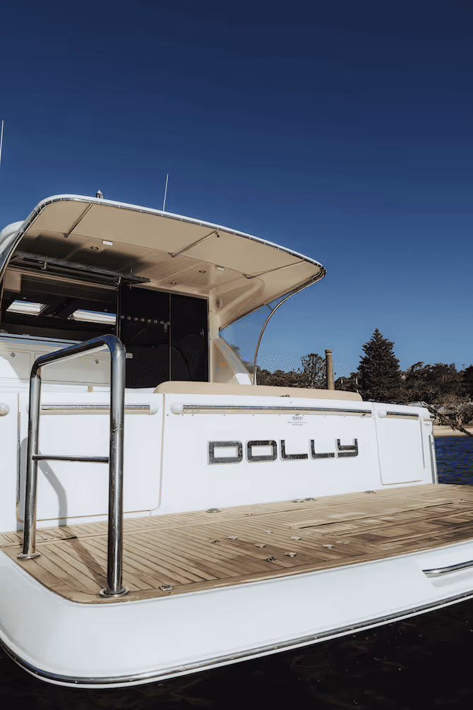Rear view of a white boat named Dolly with wooden deck and metal handrails against a clear blue sky.