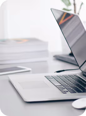 Open laptop on a desk with a blurred stack of books and tablet in the background.