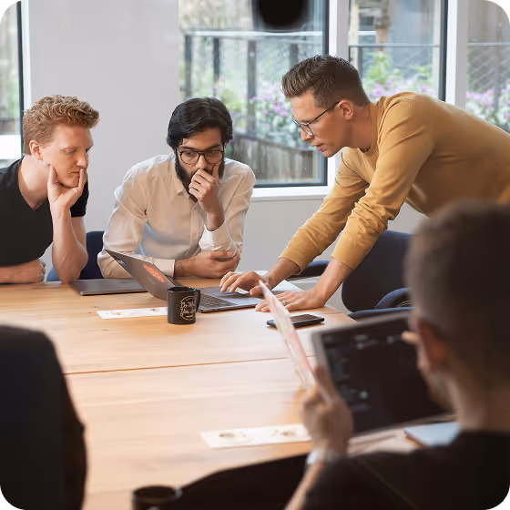 Four people collaborating around a table with laptops and documents in a well-lit office.