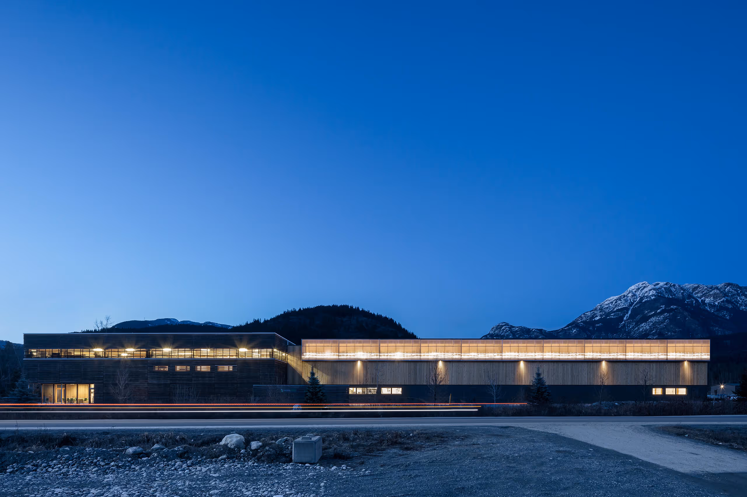 Modern illuminated building at dusk with mountains in the background and a clear blue sky.