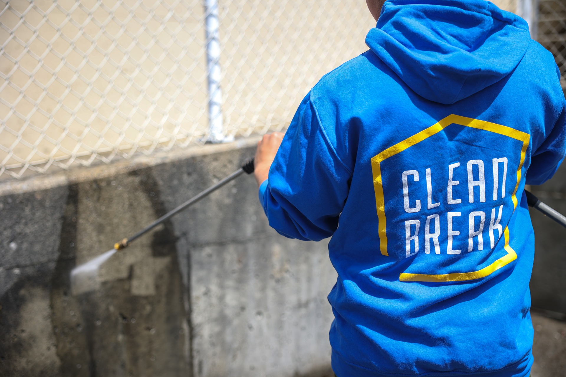 A Clean Break technician in a blue hoodie power washing a concrete wall outdoors, showcasing professional power washing services in Vancouver and Richmond.