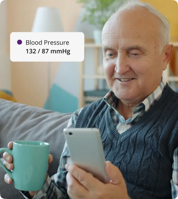 A patient at home checking his phone, with a blood pressure reading of 132/87