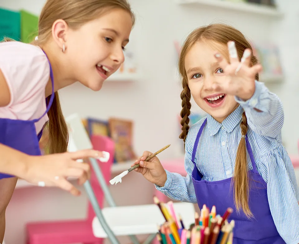 Two young girls smiling and painting with white paint in an art classroom.