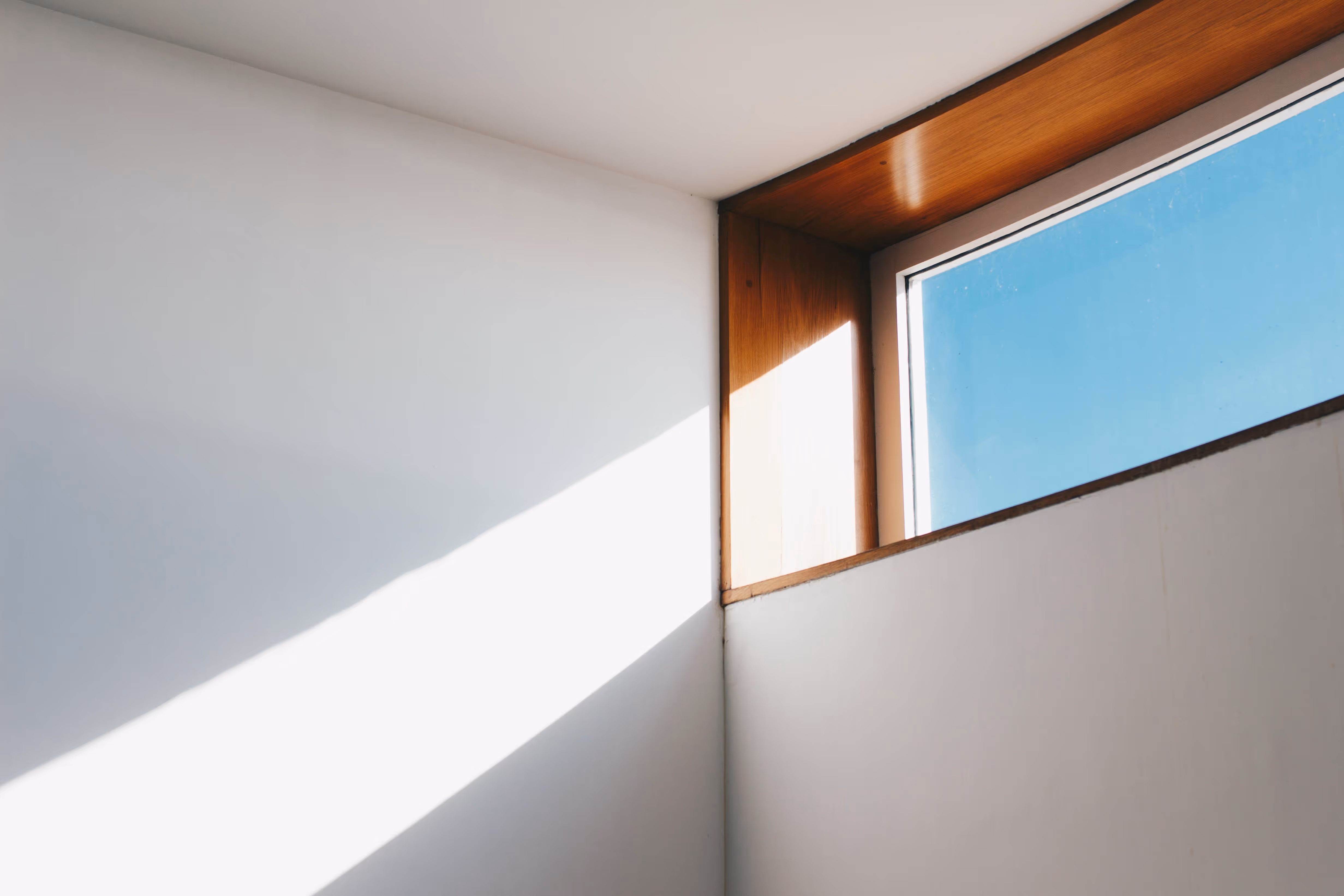 Sun shining through a top shelf window in a modern house with white walls.