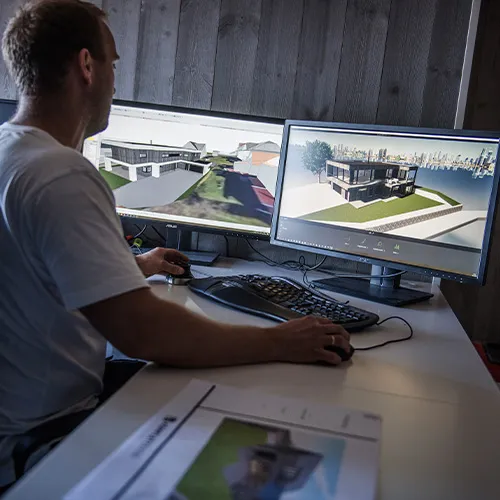 Man working on 3D architectural design of a modern house displayed on two computer monitors.