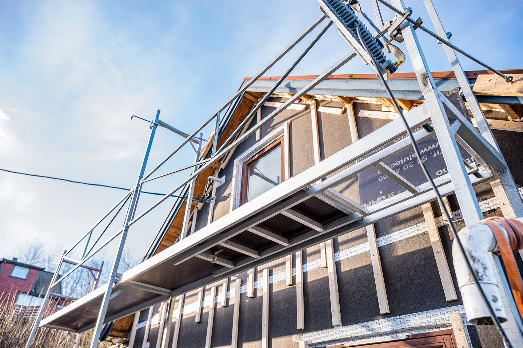 Scaffolding installed on a house under construction with wooden framing and a window.
