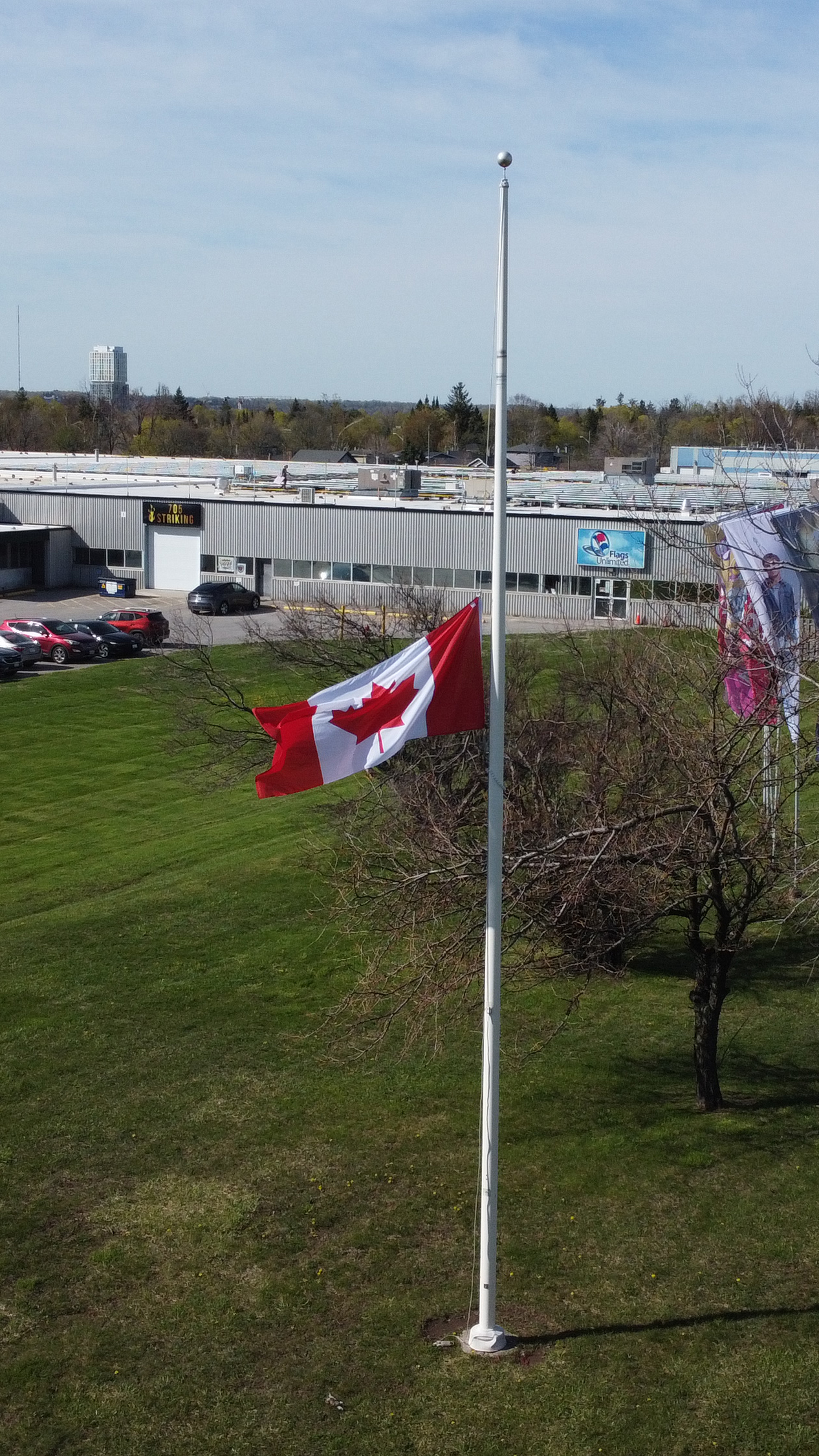 Canadian flag at half-mast on a flagpole outside an office building.