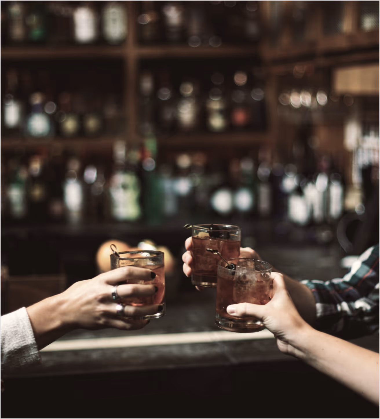 Three people toasting with cocktails at a bar.