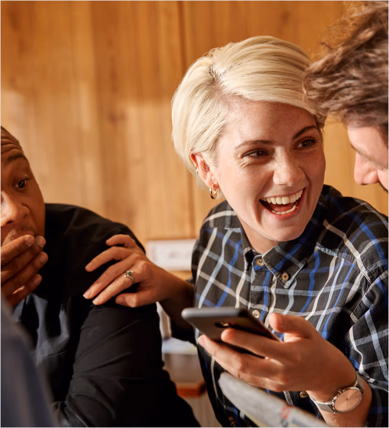 Group laughing together, one holding a phone.
