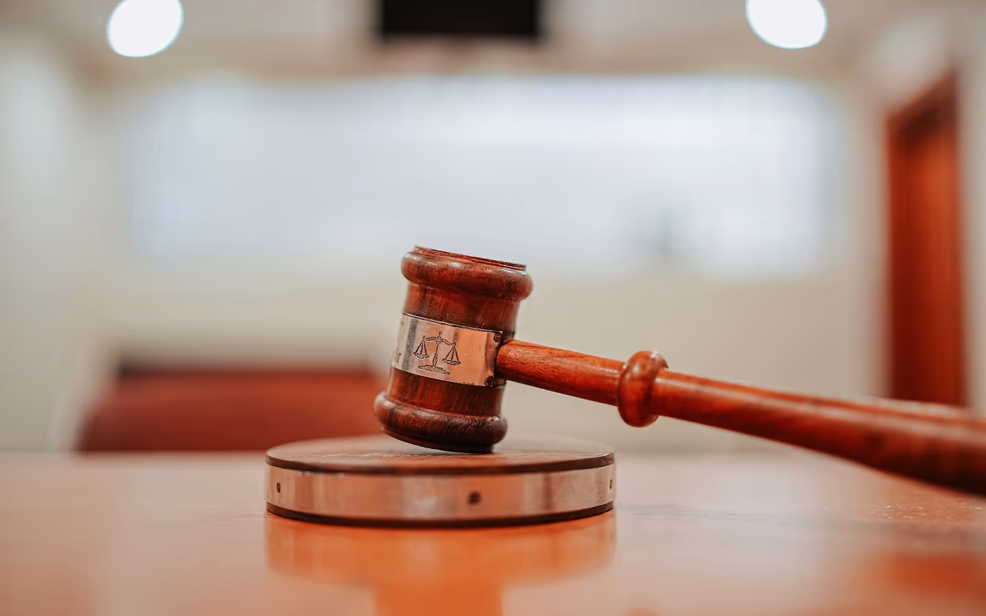 Wooden judge's gavel resting on a sound block in a courtroom setting.