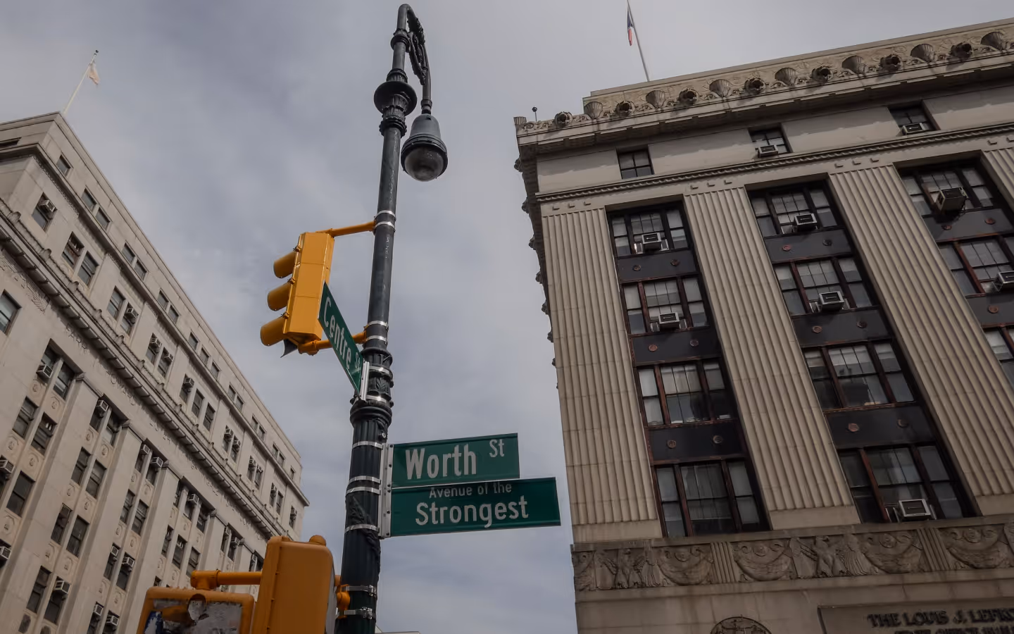 Intersection of Worth St and Centre St with a streetlamp and traffic lights in front of tall stone buildings under a cloudy sky.