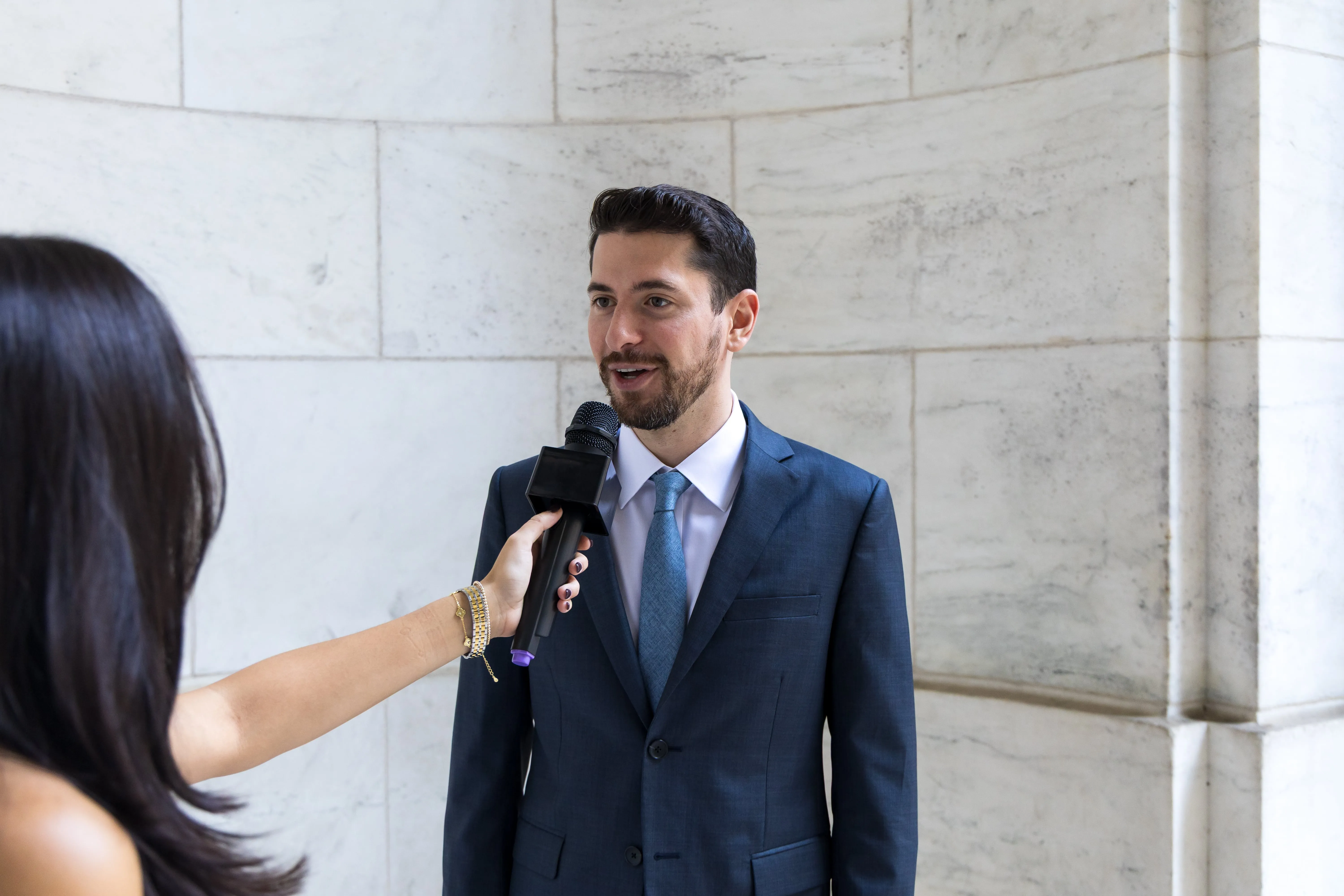 Man in a blue suit speaking into a microphone held by a woman during an interview.