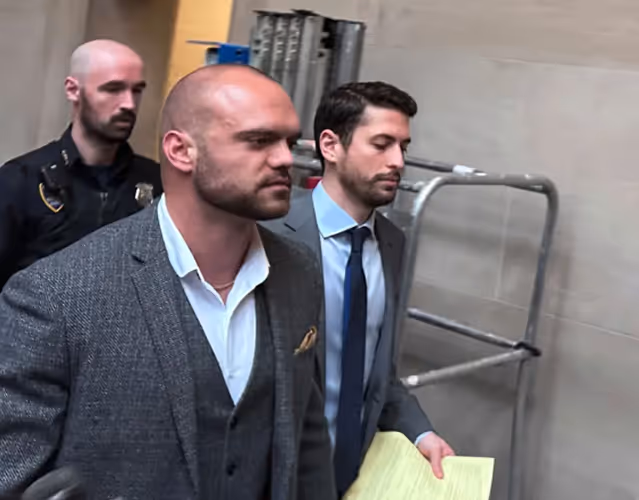 Two men in suits walking closely together, accompanied by a police officer in uniform in the background.