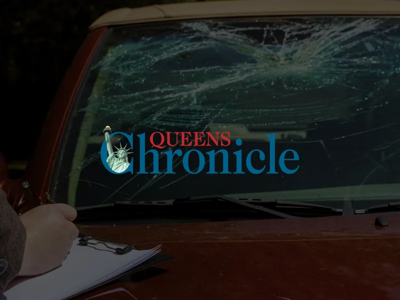 Person writing on a clipboard in front of a car with a heavily cracked windshield and Queens Chronicle logo overlay.