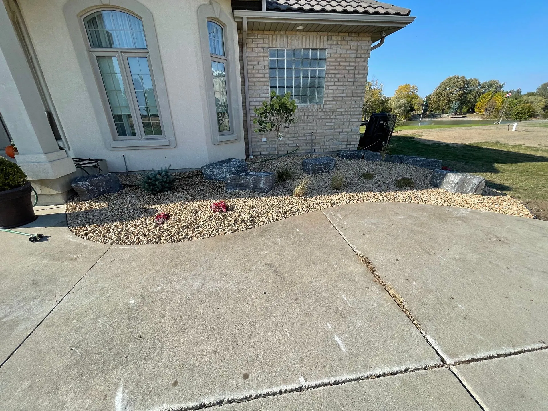 Front yard with beige gravel bed, several large rocks, small plants, and two tall windows on a light brick house.