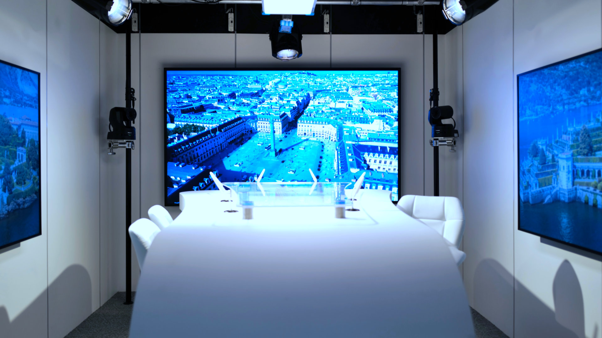 Modern conference room with white chairs and curved table facing a large screen displaying an aerial cityscape.