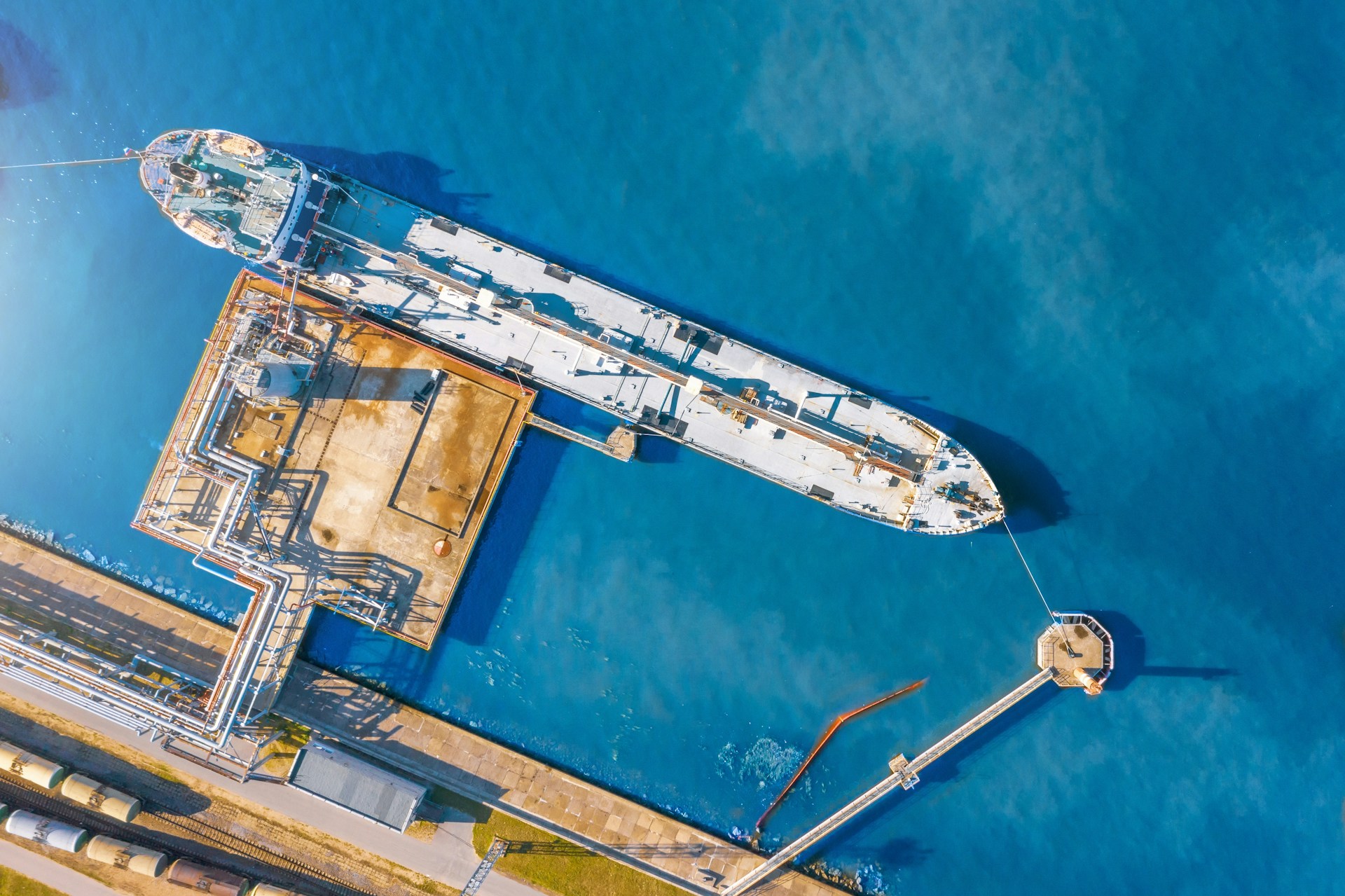 Aerial view of a large cargo ship docked at an industrial port with blue water surrounding it.