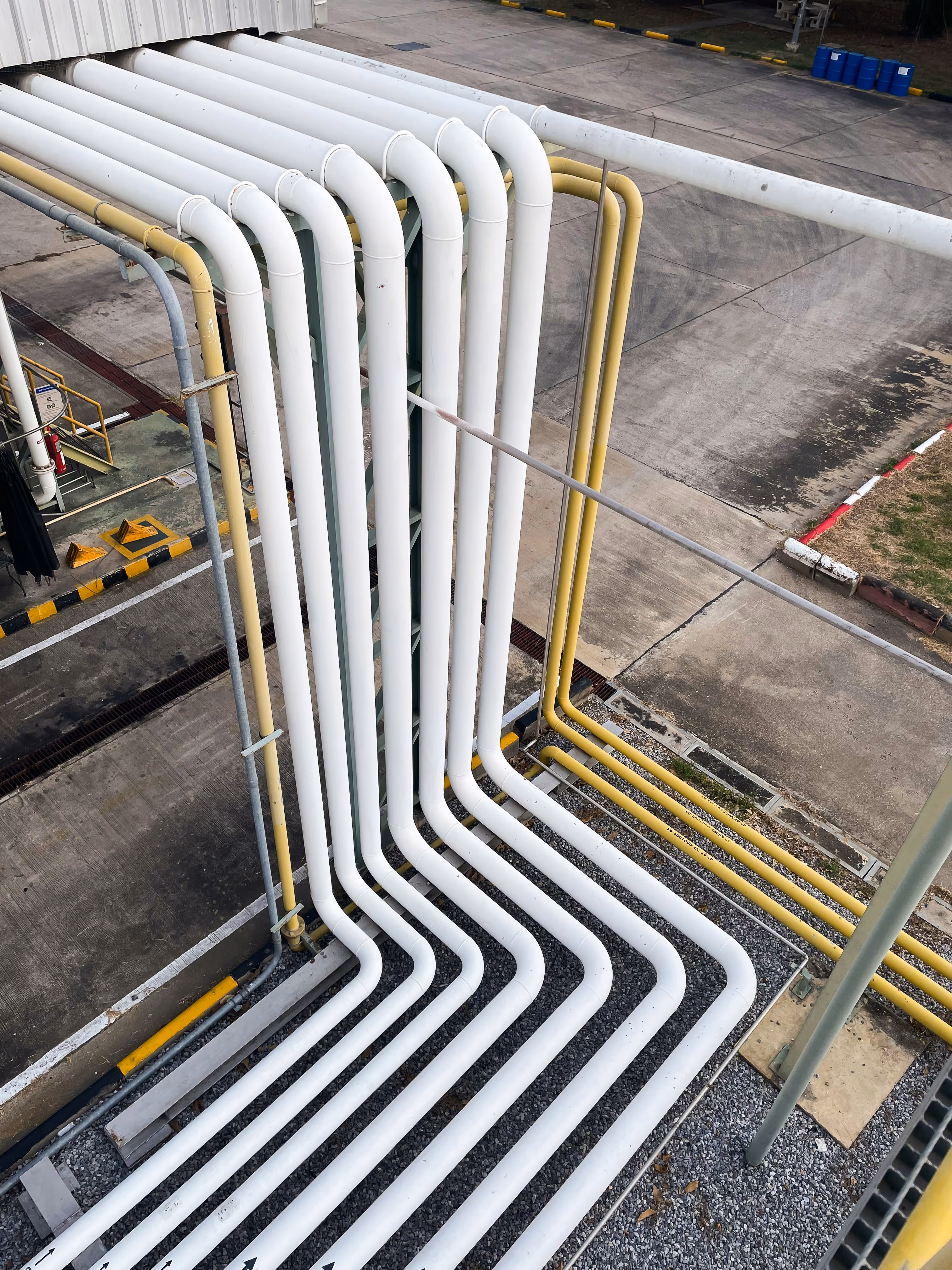 Set of large industrial white and yellow pipelines with 90-degree bends arranged in parallel on an outdoor concrete and gravel surface.
