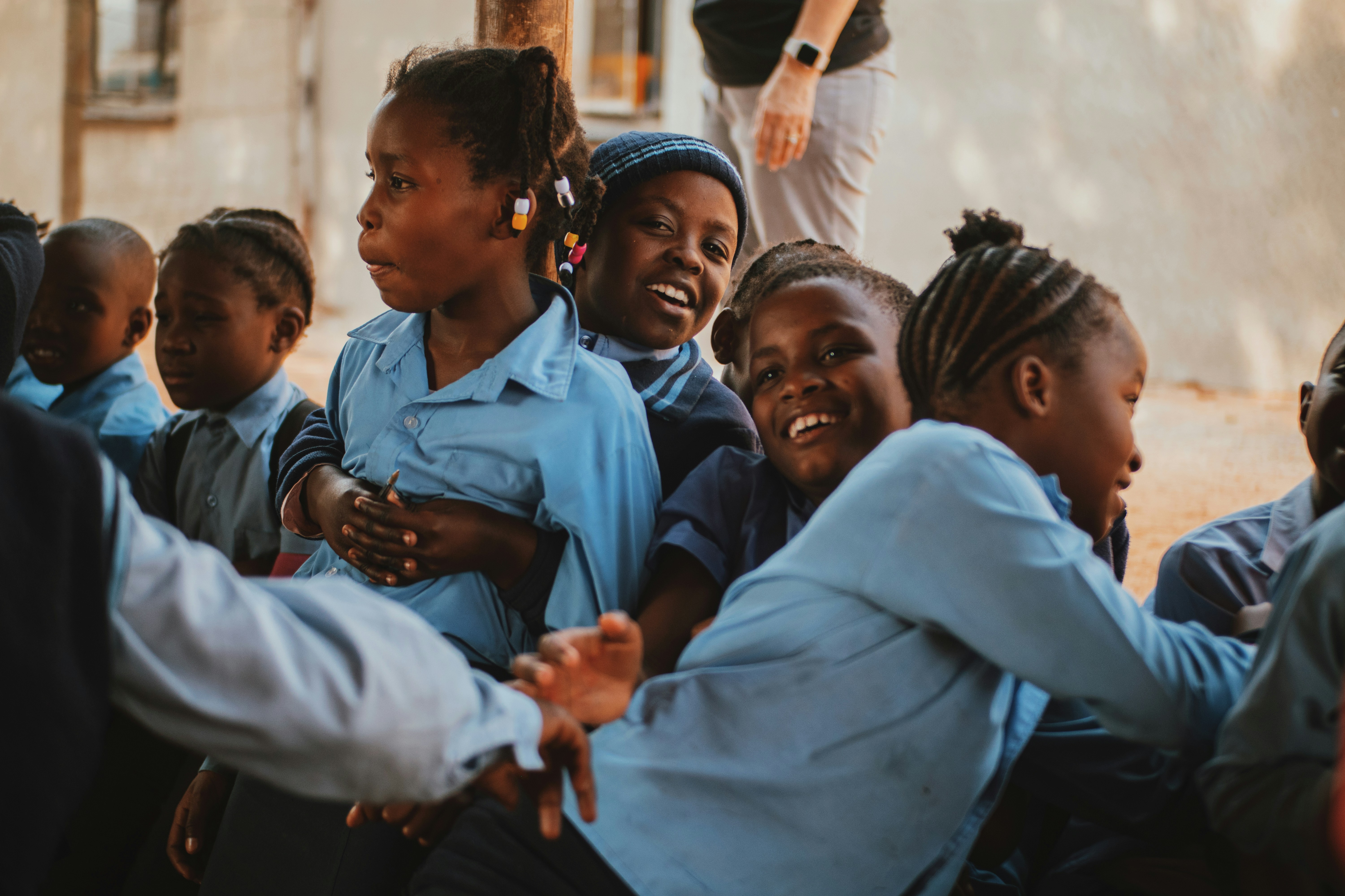 Group of smiling school children in blue uniforms playing and hugging outdoors.