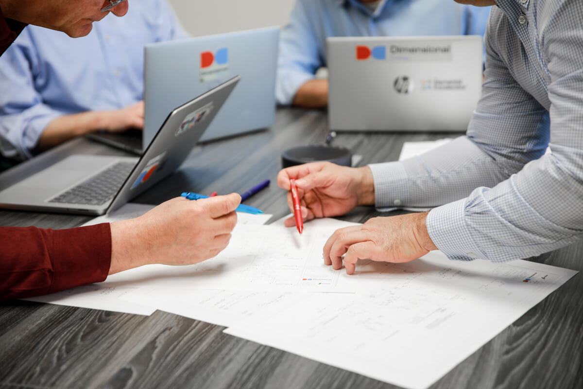 Hands holding pens poised over a technical diagram.
