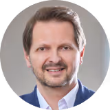 Porträt von Robert Kern mit kurzem braunem Haar und Bart, der einen blauen Anzug trägt.