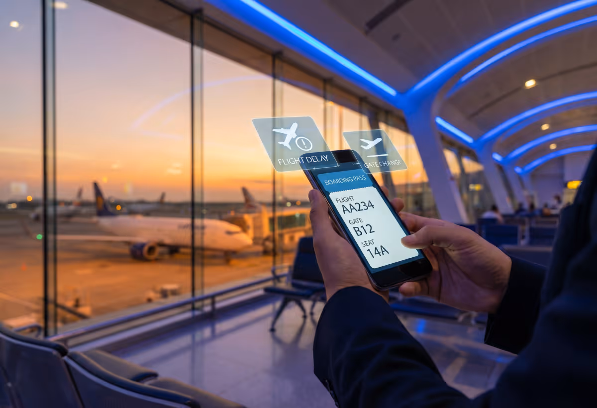 Person hält Smartphone mit digitaler Bordkarte, darunter Meldungen über Flugverspätung und Gate-Änderung, im Flughafen-Terminal bei Sonnenuntergang.