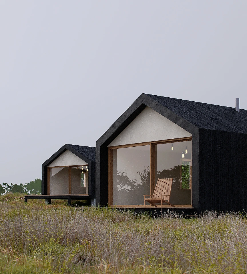 Two modern black gable-roof cabins with large glass windows, wooden chairs on the porch, set in a grassy field under an overcast sky.