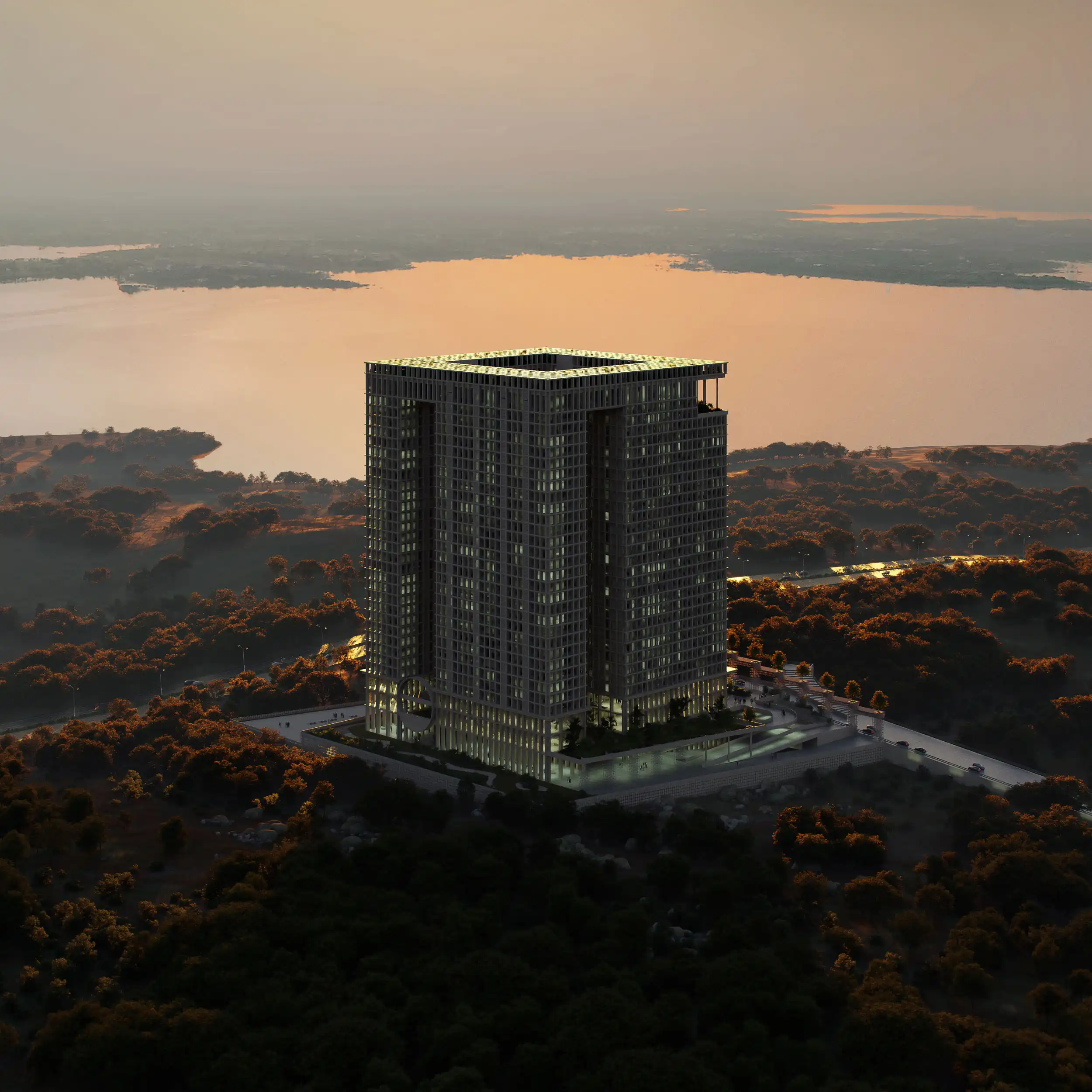 Tall modern building illuminated at dusk, surrounded by trees with a large body of water in the background.