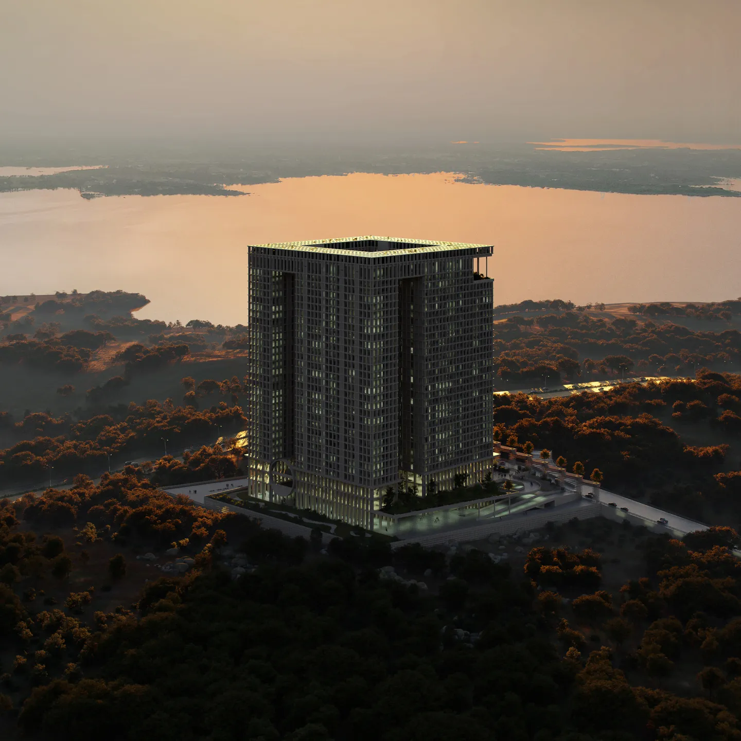 Tall modern building illuminated at dusk, surrounded by trees with a large body of water in the background.