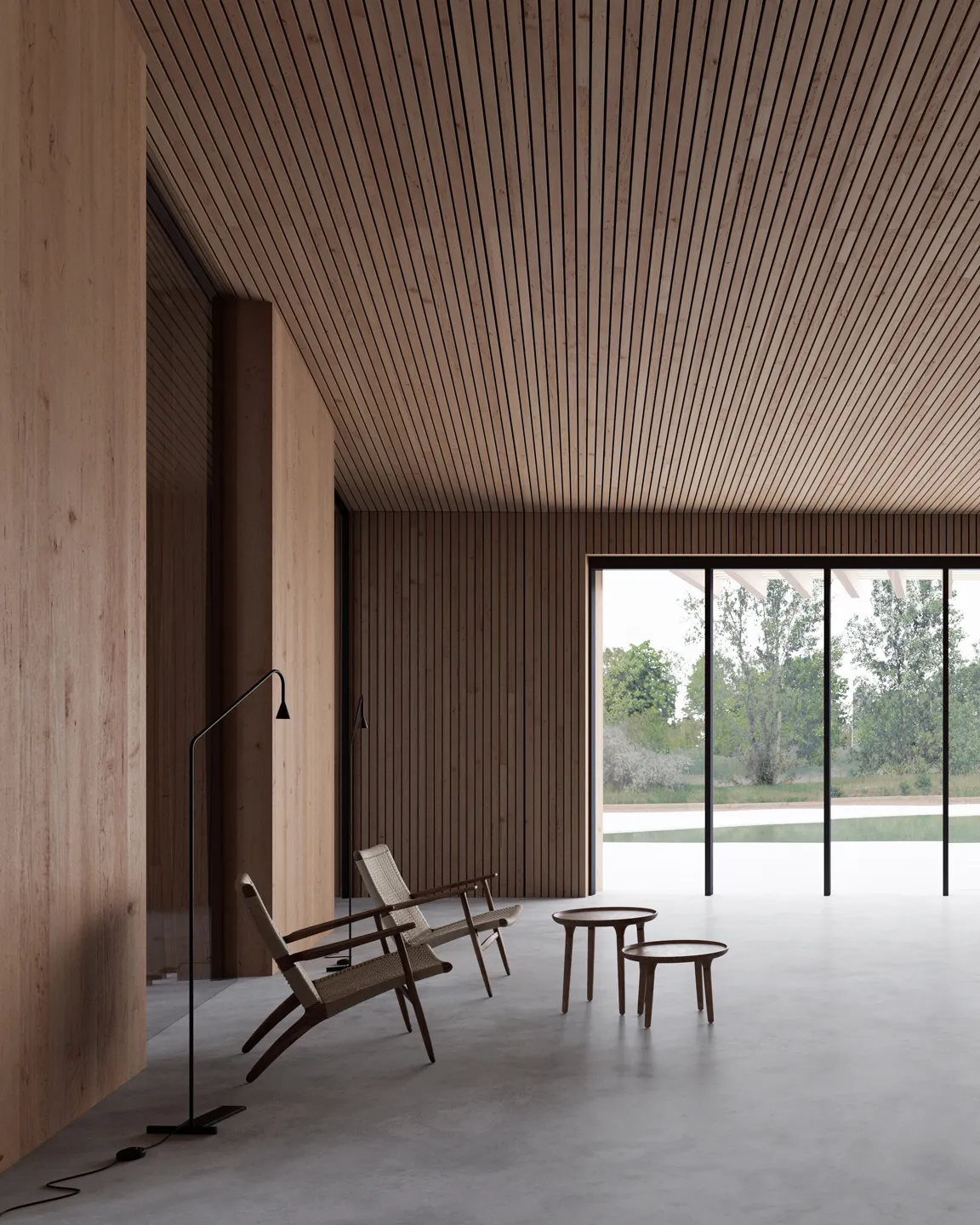 Minimalist interior with wooden slat walls and ceiling, two woven lounge chairs, two round wooden tables, and large floor-to-ceiling glass doors overlooking greenery.