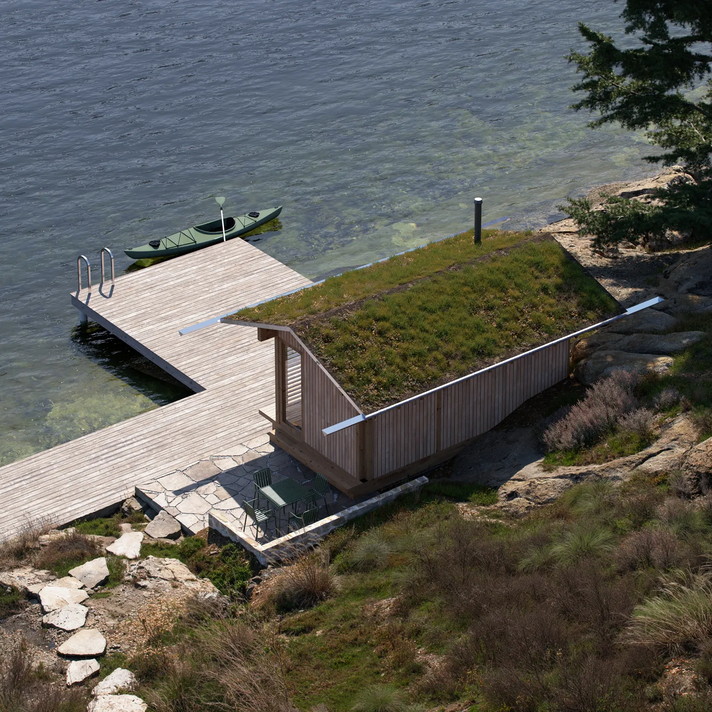 Wooden lakeside cabin with a green grass roof next to a dock with a kayak on clear water.