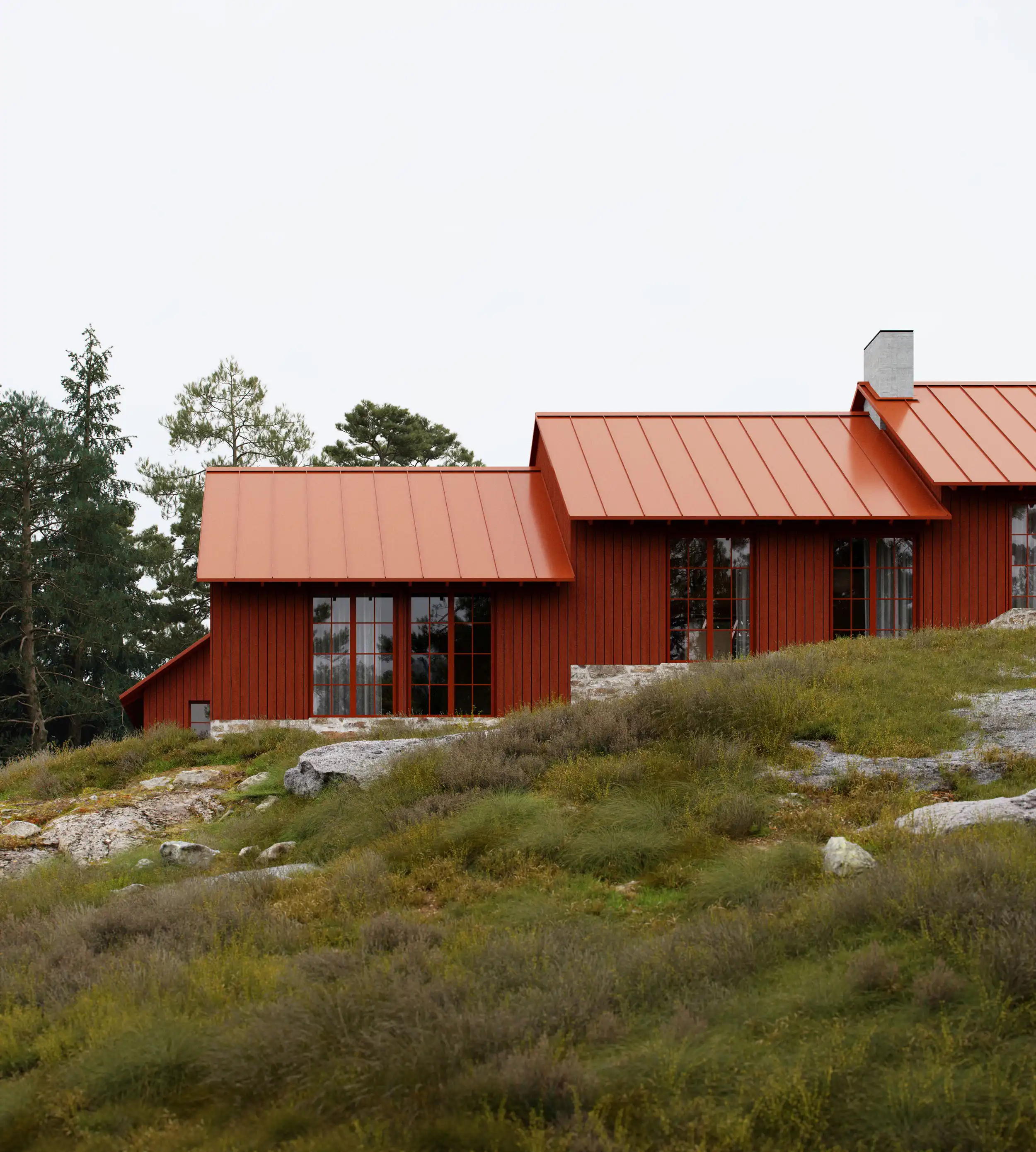 Red wooden house with a metal roof situated on a grassy hillside with rocks and trees in the background.