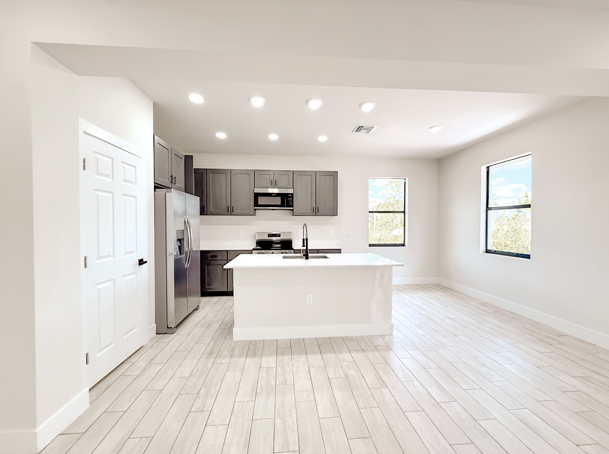 Bright modern kitchen with white island countertop, gray cabinets, stainless steel appliances, and wood-like tile flooring.