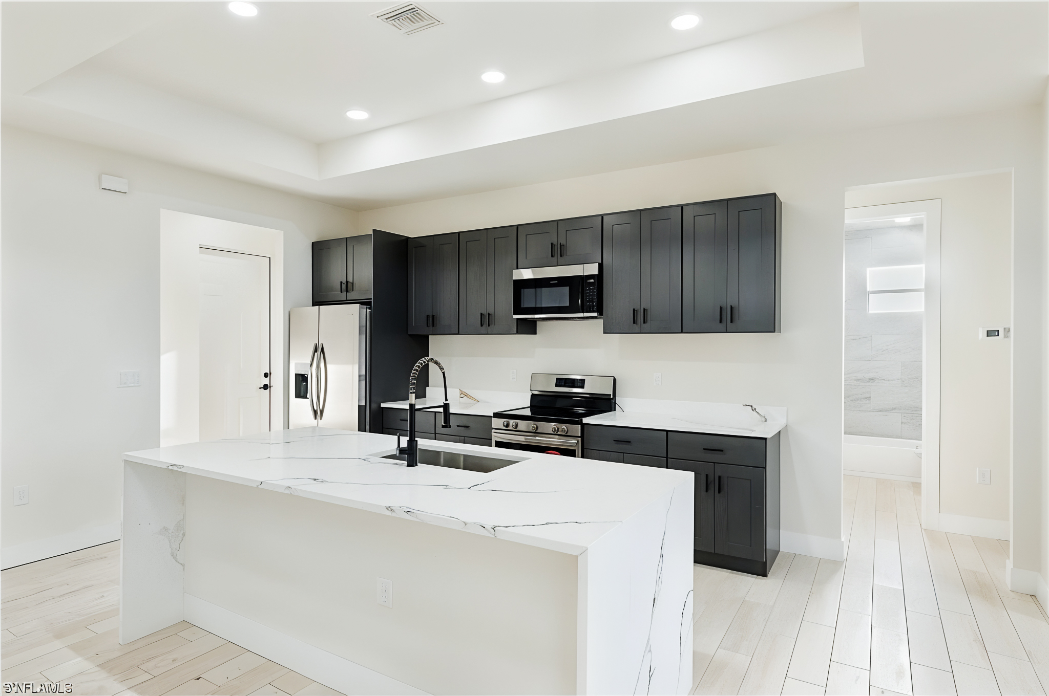 Modern kitchen with white marble island, black cabinets, stainless steel appliances, and light wood flooring.