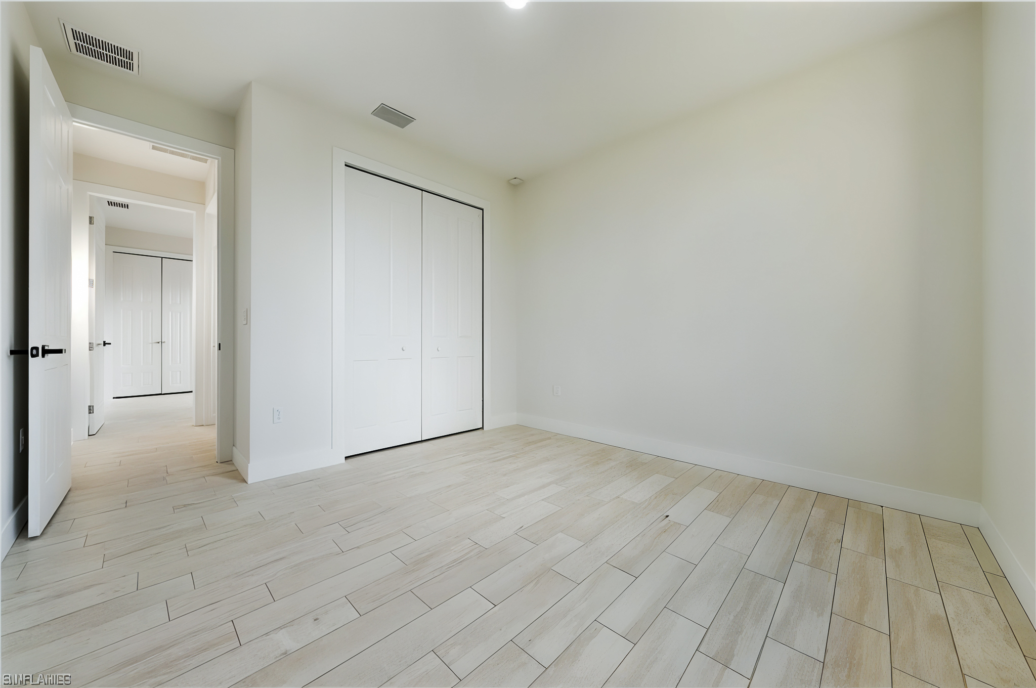 Empty room with light-colored wooden tile flooring, white walls, and a double-door closet.