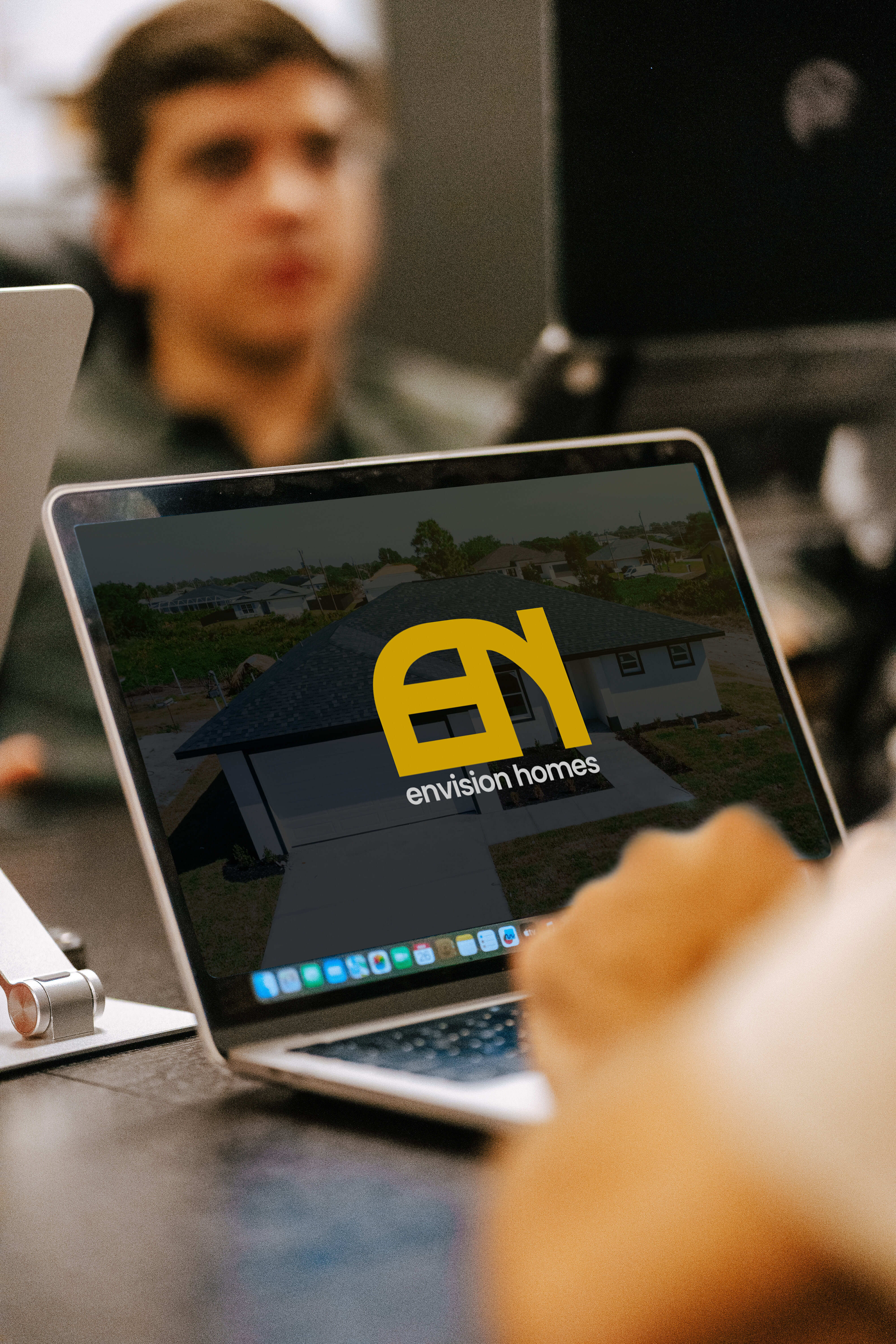 Laptop screen displaying Envision Homes logo over image of a house, with a person blurred in the background.